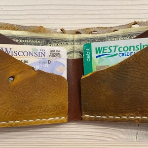 Puede incluir: Una cartera de cuero marr&oacute;n con detalles de costura blanca. La cartera est&aacute; abierta y contiene un carnet de conducir y una tarjeta de cr&eacute;dito.