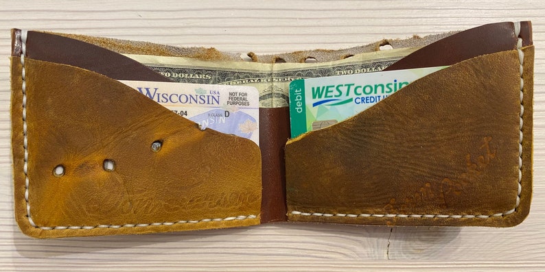 Puede incluir: Una cartera de cuero marr&oacute;n con detalles de costura blanca. La cartera est&aacute; abierta y contiene un carnet de conducir y una tarjeta de cr&eacute;dito.