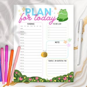 May include: A colorful planner page with the text "PLAN for today" in blue and pink. The page includes sections for a schedule, to-do list, notes, and gratitude. Decorative elements include a frog, bee, and flowers. Colored markers and a pen are visible.