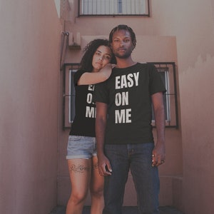 May include: A couple wearing matching black t-shirts with white text. The man's shirt says "EASY ON ME" and the woman's shirt says "EASY ON ME".