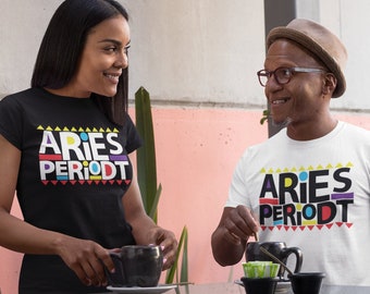 Op de afbeelding: Twee mensen dragen zwarte en witte T-shirts met de tekst "Aries PeriodT" in kleurrijke blokletters. De shirts hebben een geometrisch patroon rond de tekst.