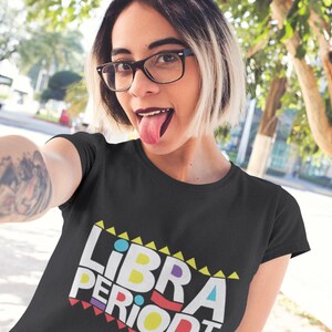 Puede incluir: Camiseta negra con un gr&aacute;fico colorido que dice "LIBRA PERIODT" en un estilo retro.