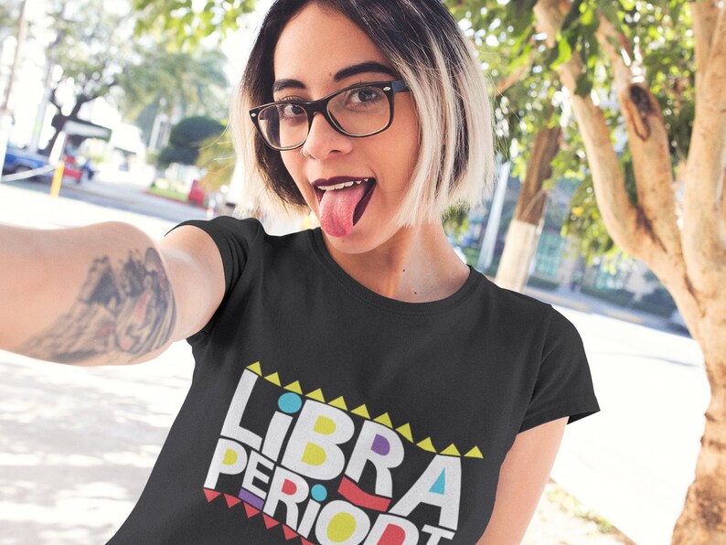 Puede incluir: Camiseta negra con un gr&aacute;fico colorido que dice "LIBRA PERIODT" en un estilo retro.