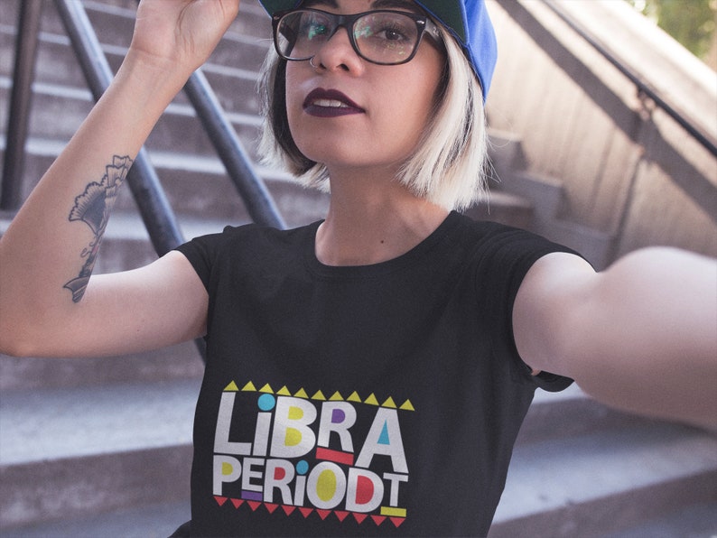 Puede incluir: Una camiseta negra con un gr&aacute;fico colorido que dice "LIBRA PERIODT" en un estilo retro.