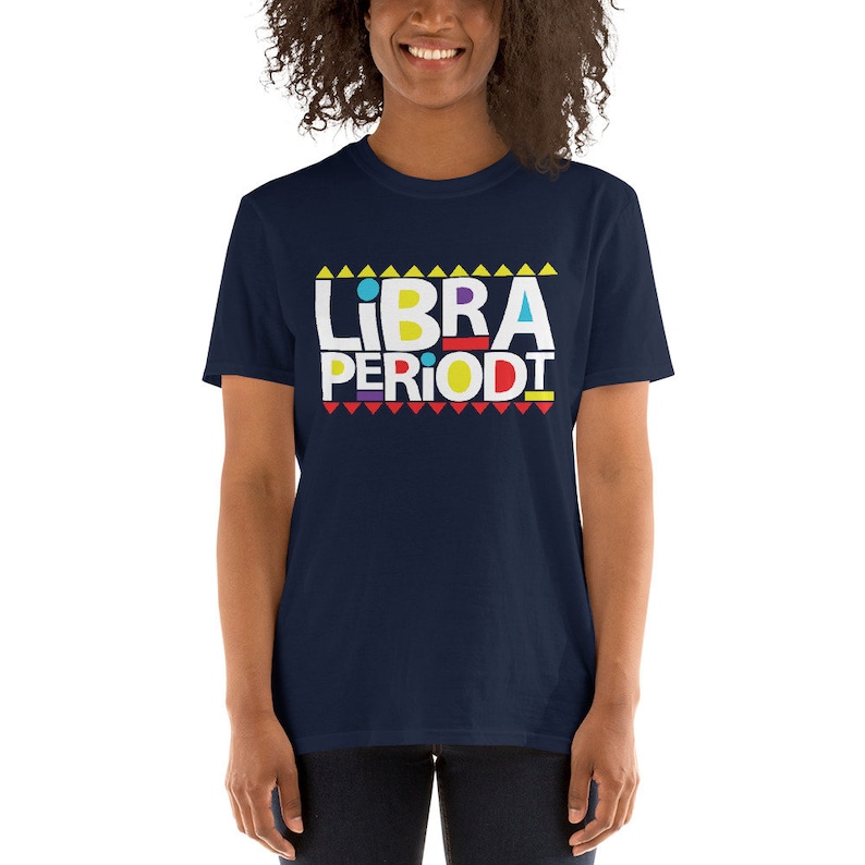 Puede incluir: Una camiseta azul marino con un gr&aacute;fico blanco que dice "LIBRA PERIODT" en letras may&uacute;sculas de colores. El gr&aacute;fico est&aacute; rodeado de tri&aacute;ngulos amarillos en la parte superior y tri&aacute;ngulos rojos en la parte inferior.
