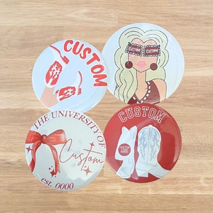 May include: Four round, custom-designed buttons. One features a woman with sunglasses, another has cowboy boots, and a third displays a bow and the text "The University of Custom". The fourth button has cowboy boots and the text "Custom Logo Here!"