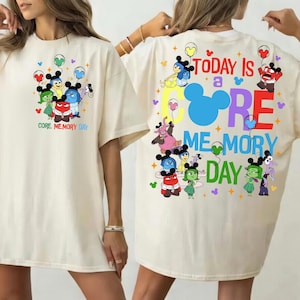 May include: An ivory t-shirt featuring Inside Out characters with Mickey ears and balloons. The front has a small graphic with the text "CORE MEMORY DAY". The back features a large graphic with the text "TODAY IS A CORE MEMORY DAY".