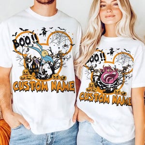 May include: Two white short-sleeve t-shirts featuring a Halloween-themed graphic. The design includes a mouse-ear silhouette, a spider web, bats, a witch, pumpkins, and the text "BOO!!" and "CUSTOM NAME" in orange, black, and purple colors.