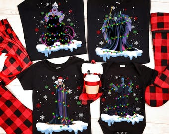Camiseta con los villanos de Disney: Reina Malvada, Hades, Maléfica, Úrsula, disfraz de Papá Noel, luces navideñas y copos de nieve. Camisetas navideñas a juego de Disneyland.