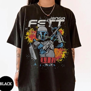 Puede incluir: Camiseta negra con un gráfico de Jango Fett de Star Wars. El diseño incluye el texto "Jango Fett" en blanco, con una ilustración del personaje en azul, gris y rojo. La camiseta tiene cuello redondo.