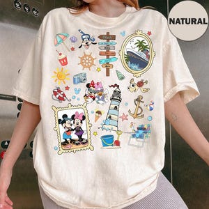 May include: Cream-colored t-shirt featuring a collage of beach-themed illustrations. Includes Mickey and Minnie Mouse, a cruise ship, lighthouse, and various nautical elements. The word "NATURAL" is printed on the upper right.
