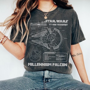 May include: Dark gray t-shirt featuring a detailed blueprint of the Millennium Falcon from Star Wars. The shirt includes the text "STAR WARS YT-1300 TRANSPORT" and "MILLENNIUM FALCON" in white lettering. The design also includes technical specifications.