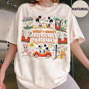 May include: Cream-colored t-shirt featuring a colorful graphic of Mickey and Minnie Mouse on a runaway railway. The design includes various Disney characters, a red car, and the text "Mickey & Minnie's Runaway Railway."