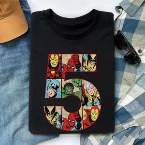 May include: A black crew neck t-shirt featuring a large graphic of the number five. The number is filled with comic book style illustrations of various superheroes, including Iron Man, Spider-Man, Wolverine, Captain America, Hulk, and Thor.