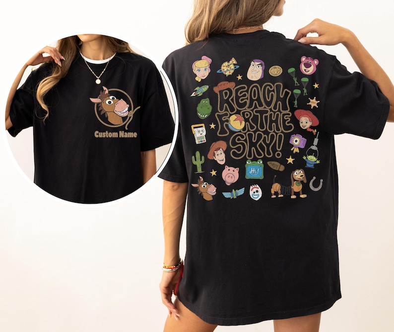 May include: A black t-shirt featuring a front graphic of a horse head inside a rope circle with the text Custom Name. The back displays various cartoon character icons and the text REACH FOR THE SKY! in a large, bold, brown, wavy font.