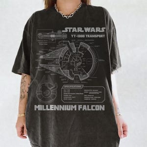 Puede incluir: Una camiseta de manga corta gris carbón con un gráfico de plano técnico en gris claro del transporte Star Wars Millennium Falcon YT-1300. El diseño incluye esquemas detallados, especificaciones técnicas y el texto Millennium Falcon.