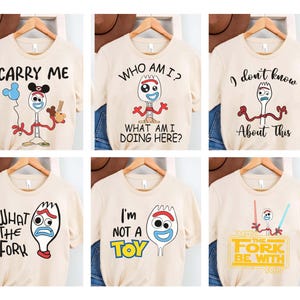 May include: Six cream-coloured t-shirts with cartoon graphics and text. The designs feature a fork-like character with phrases like "CARRY ME," "WHO AM I?" and "MAY THE FORK BE WITH YOU." The shirts are displayed on wooden hangers.