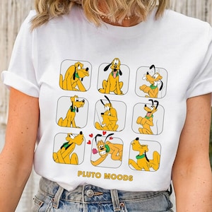 Könnte beinhalten: Weißes T-Shirt mit einem Raster von Pluto-Illustrationen, die jeweils eine andere Stimmung zeigen. Der Cartoon-Hund ist gelb mit schwarzen Ohren und einem grünen Kragen. Der Text "PLUTO MOODS" ist gelb gedruckt.