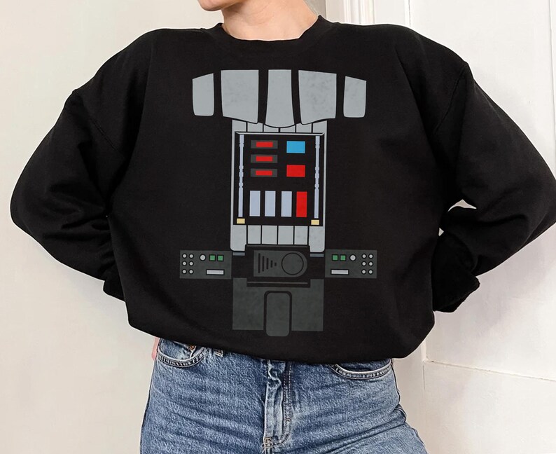Op de afbeelding: Een zwart sweatshirt met lange mouwen en een grafische print op de borst die een mechanisch bedieningspaneel nabootst. Het ontwerp bevat grijze rechthoekige vormen, een centraal raster met rode, blauwe en witte vierkanten en zijpanelen.