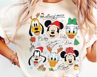 May include: Cream-colored t-shirt featuring cartoon faces of Mickey Mouse, Pluto, Goofy, Donald Duck, Daisy Duck, and Minnie Mouse, all in festive holiday attire. The shirt includes the characters' names and holiday-themed graphics.