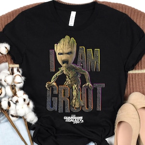 May include: Black t-shirt featuring a graphic of Groot from Guardians of the Galaxy Vol. 2. The text "I AM GROOT" is displayed in colorful, outlined letters. The shirt is a crew neck.