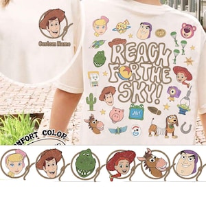 May include: A cream-colored t-shirt featuring a small graphic of Woody on the front with the text Custom Name. The back displays a large collage of Toy Story characters and icons with the text REACH FOR THE SKY! in a rope-style font.