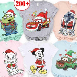 Op de afbeelding: Collectie kerst-t-shirts met stripfiguren. Ontwerpen omvatten een alien, Bliksem McQueen, R2-D2, een kat, Mickey Mouse en Mater, allemaal met kerstmutsen en feestelijke lichtjes. De shirts zijn in verschillende kleuren.