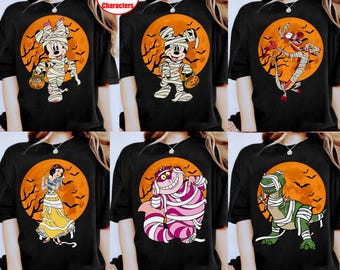 Op de afbeelding: Een collectie van zes zwarte t-shirts, elk met een ander stripfiguur gewikkeld in witte mummiebandages. De figuren staan tegen een achtergrond van een grote oranje volle maan met silhouetten van vliegende vleermuizen en takken.