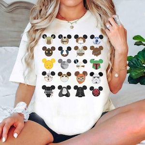 May include: White crew neck t-shirt with a grid of cartoon character faces designed as Mickey Mouse ears. Characters include Yoda, Darth Vader, and R2-D2. The shirt is a casual style.