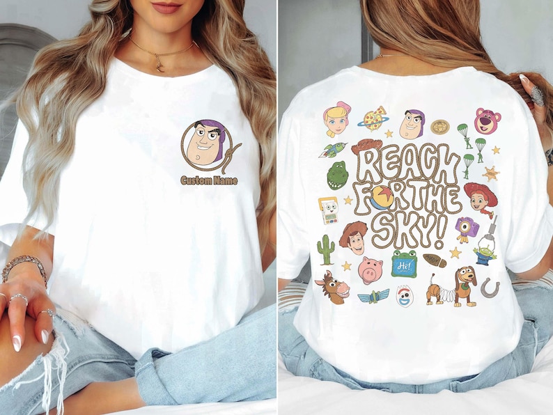 May include: A white t-shirt featuring a small Buzz Lightyear graphic on the front chest with the text Custom Name. The back displays a large colorful collage of Toy Story characters and the text REACH FOR THE SKY in a brown bubble font.