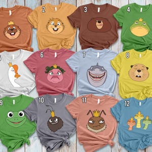 Puede incluir: Una colección de doce camisetas de manga corta en varios colores, cada una con una cara de animal de dibujos animados con una corona. Las camisetas incluyen un castor, un oso, una rana, un tiburón, un ganso y una hormiga.