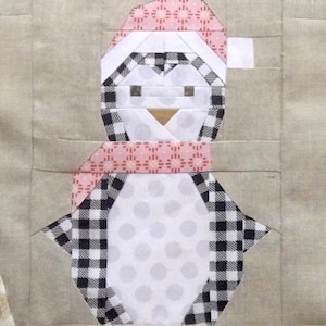 Puede incluir: Un pingüino blanco con un patrón de cuadros blanco y negro, que lleva una bufanda de patrón rosa y blanco y un sombrero de patrón rosa y blanco.