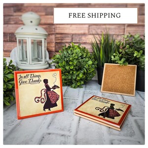 May include: Two ceramic coasters with a red border and a silhouette of a woman carrying a pie. The text on the coasters reads "In all things, Give Thanks".