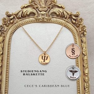 Könnte beinhalten: Goldkette mit einem runden Anhänger, der den griechischen Buchstaben Psi zeigt, das Symbol für Psychologie. Der Anhänger ist mit dem Wort "Psychologie" graviert. Die Kette wird auf einem goldenen, verzierten Rahmen mit dem Text "STUDIENGANG HALSKEKETTE CECE'S CARIBBEAN BLUE" präsentiert.