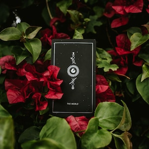 May include: A black tarot card with white illustrations depicting a circle with a globe inside, a star, and a wand. The card reads "THE WORLD" at the bottom.
