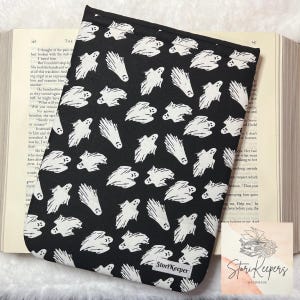 May include: Black book sleeve with a white ghost pattern. The sleeve has the text "StoriKeeper" printed on the bottom.