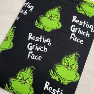 May include: Black fabric with a green Grinch face pattern. The fabric has the text "Resting Grinch Face" repeated throughout. The fabric is made by Stori'Keeper.