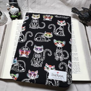 May include: Black book cover with a repeating pattern of colorful sugar skull cats. The text "Story Keeper Handmade" is printed on the bottom right corner of the cover.