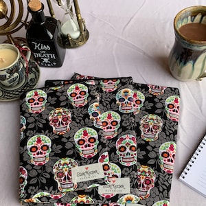 May include: Three black fabric pouches with a colorful sugar skull pattern. Each pouch has a white label with the text "StoriKeeper Handmade".