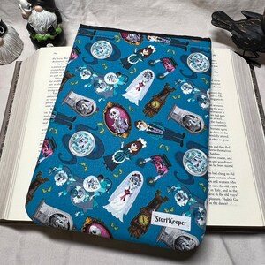 May include: A blue book cover with a repeating pattern of ghosts, clocks, and skeletons. The text "StoryKeeper" is printed on the bottom right corner of the cover.