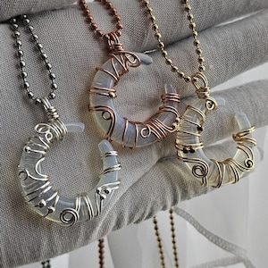 May include: Three crescent moon necklaces with wire-wrapped designs. The necklaces feature silver, copper, and gold-coloured wire, each with a different chain. The moon pendants have a pearlescent, opalescent appearance.
