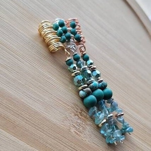 May include: A set of three gold hair coils with green and blue beads. The coils are made of metal and have a springy design. The beads are various shades of green and blue, and some are faceted.