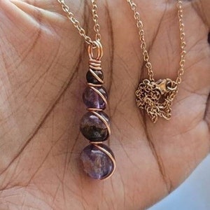 May include: A gold chain necklace with a pendant made of four amethyst stones wrapped in copper wire.