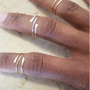 May include: Three gold rings with a simple, minimalist design. The rings are worn on the fingers of a person's hand.