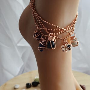 May include: Copper anklet with multiple strands of beads and dangling wire-wrapped stones in shades of blue, black, and white.