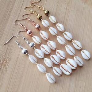 May include: Three pairs of long, dangling earrings with white cowrie shells and gold, rose gold, and silver beads.