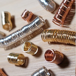 Może przedstawiać: Zbiór metalowych spięć do włosów w kształcie spirali w odcieniach srebra, złota i miedzi. Spinki są ułożone na drewnianej powierzchni.