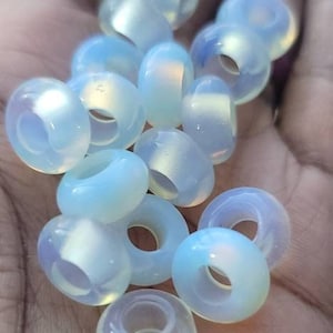 May include: A collection of iridescent opalite beads with a hole in the center. The beads are a light blue color with a pearly sheen.