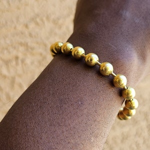 Op de afbeelding: Een gouden armband met ronde, gladde kralen. De armband wordt om de pols gedragen.