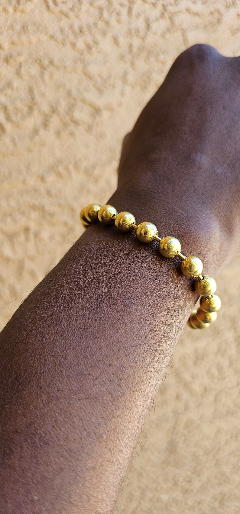 Op de afbeelding: Een gouden armband met ronde, gladde kralen. De armband wordt om de pols gedragen.